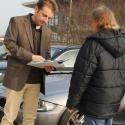 Mann zeigt einemn Mann vor Auto ein Papier